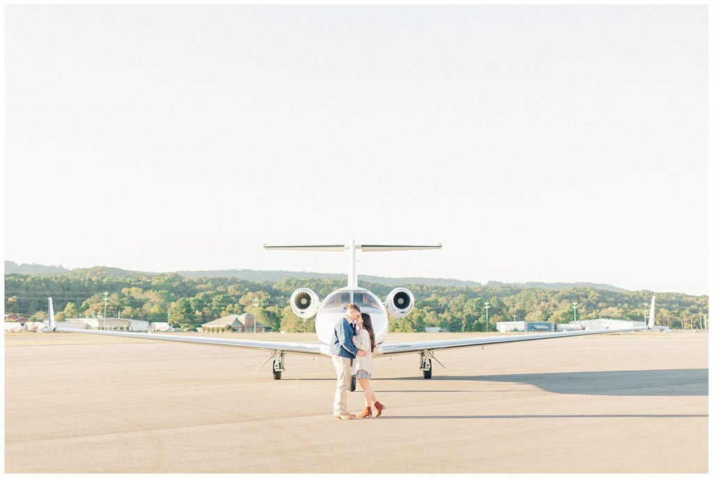 couple snuggling in front of private jet at engagement session